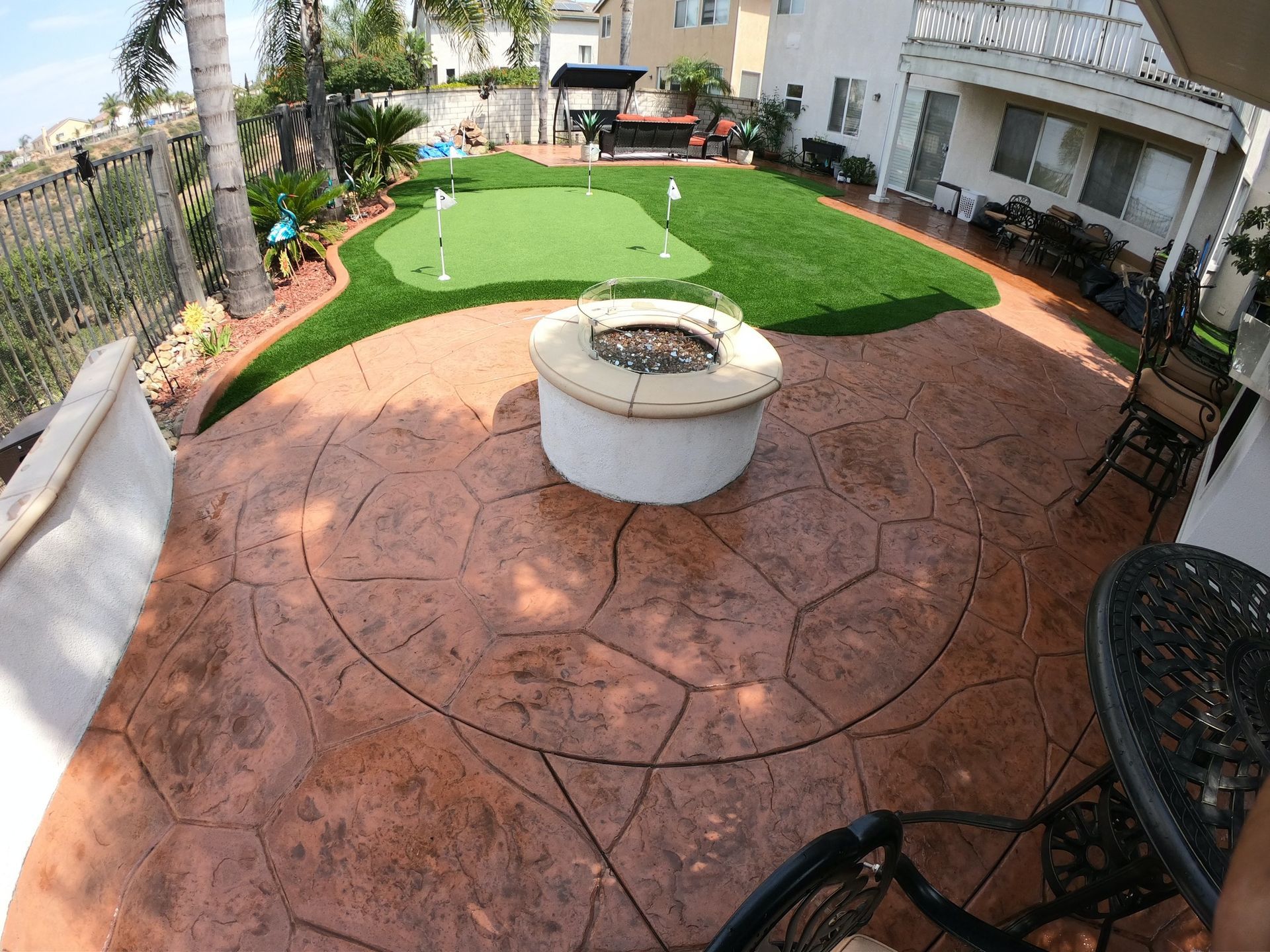 Backyard patio with fire pit, putting green, and house.