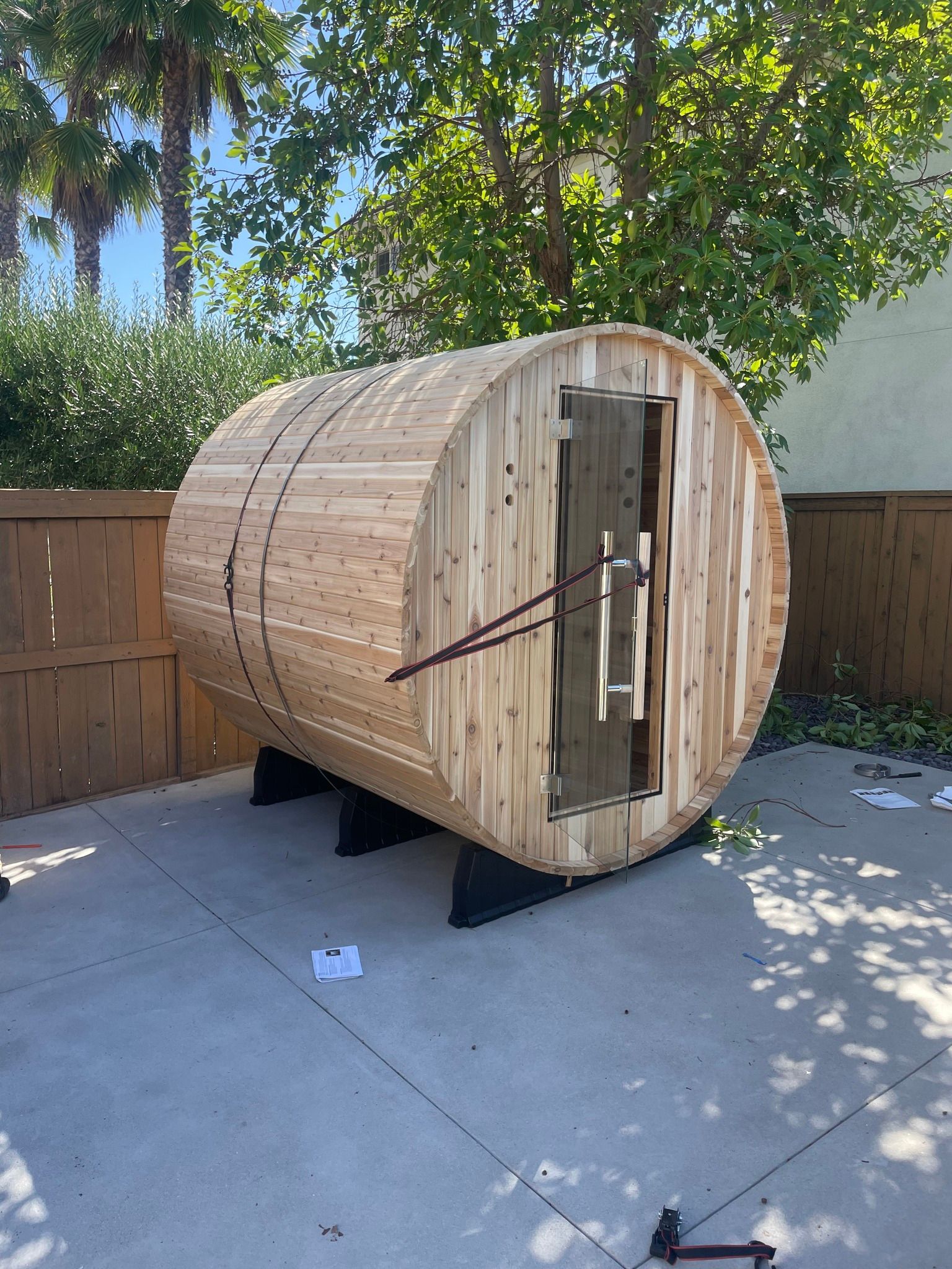 Wooden barrel sauna on black supports, with an open door in a backyard.
