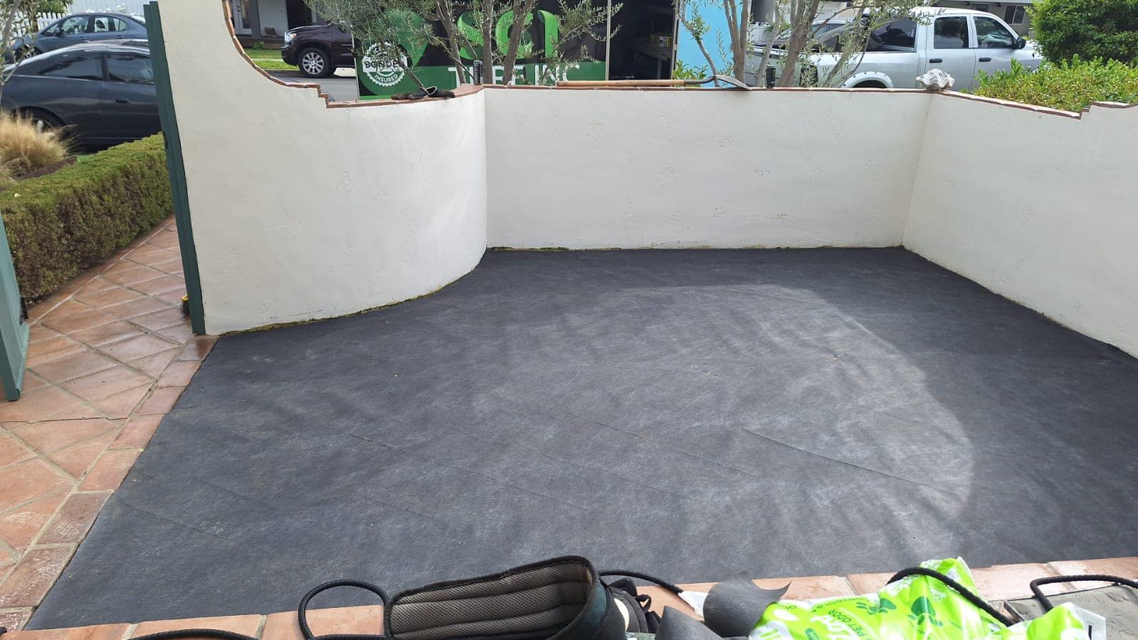 Black asphalt driveway framed by brick and white walls; plants in background.