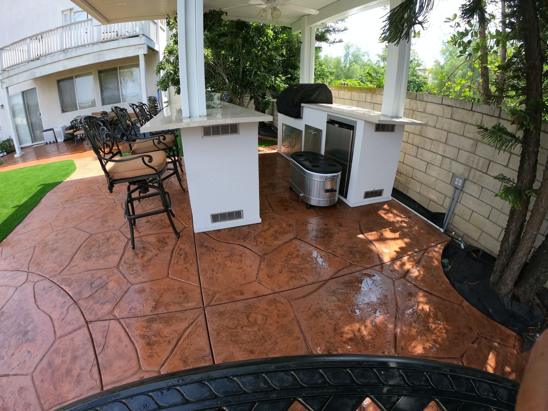 Patio with stamped concrete, outdoor kitchen with grill and bar seating under a covered structure.