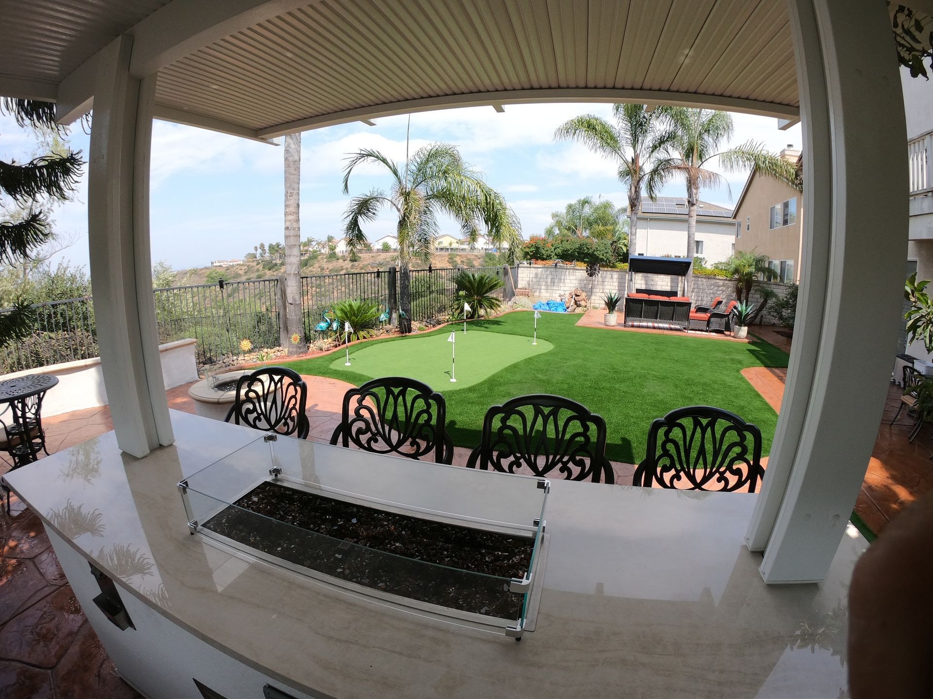 Outdoor bar with view of a putting green, palm trees, and houses on a sunny day.