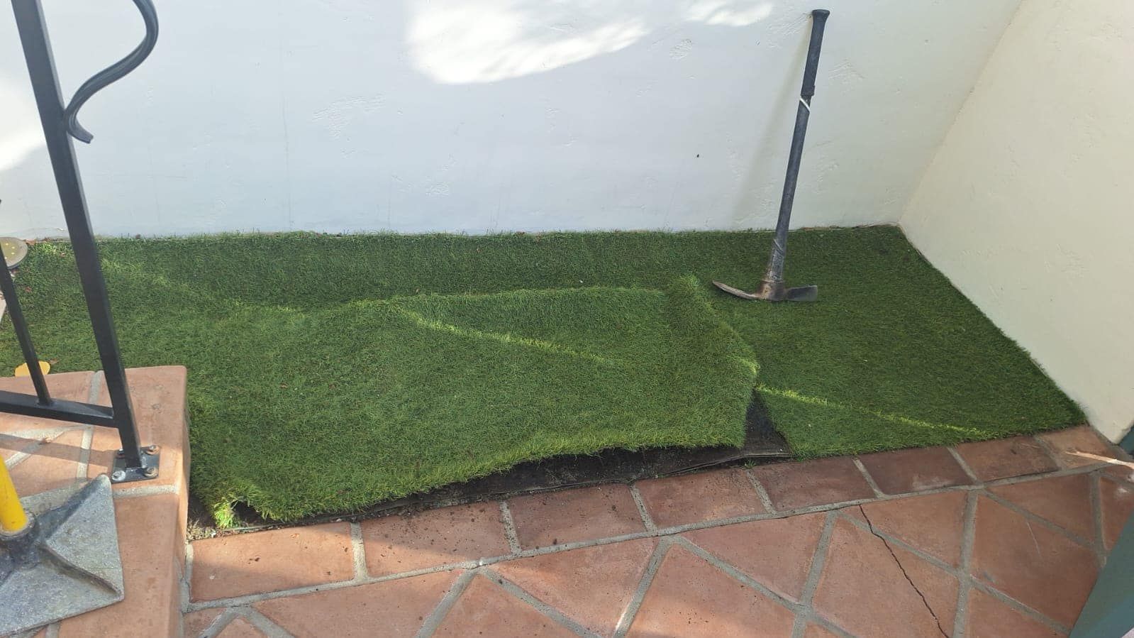 Artificial turf partially covering a small landing area in front of stairs, with tools leaning nearby.