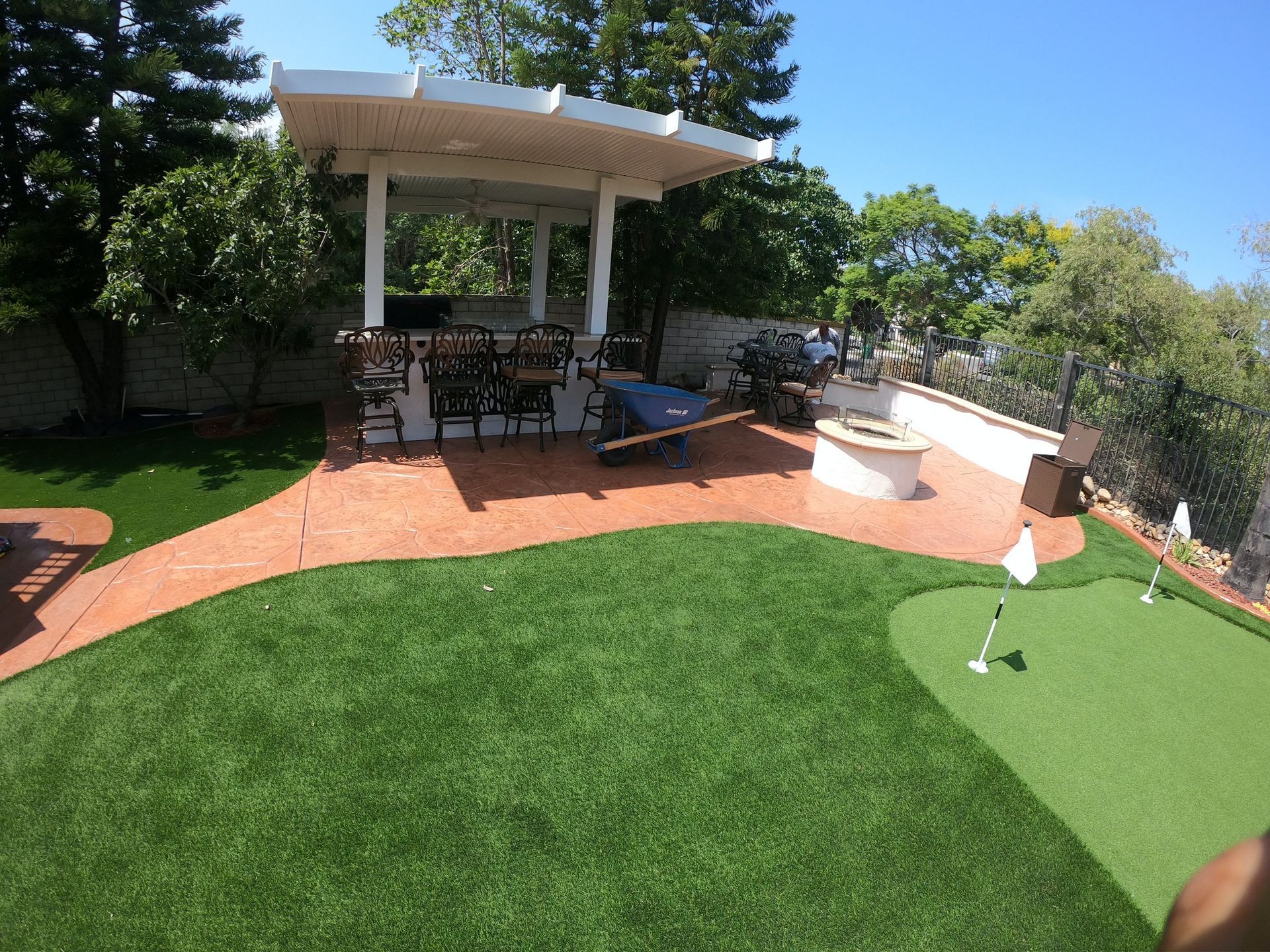 Backyard with putting green, patio with seating, pergola, fire pit, and synthetic turf.