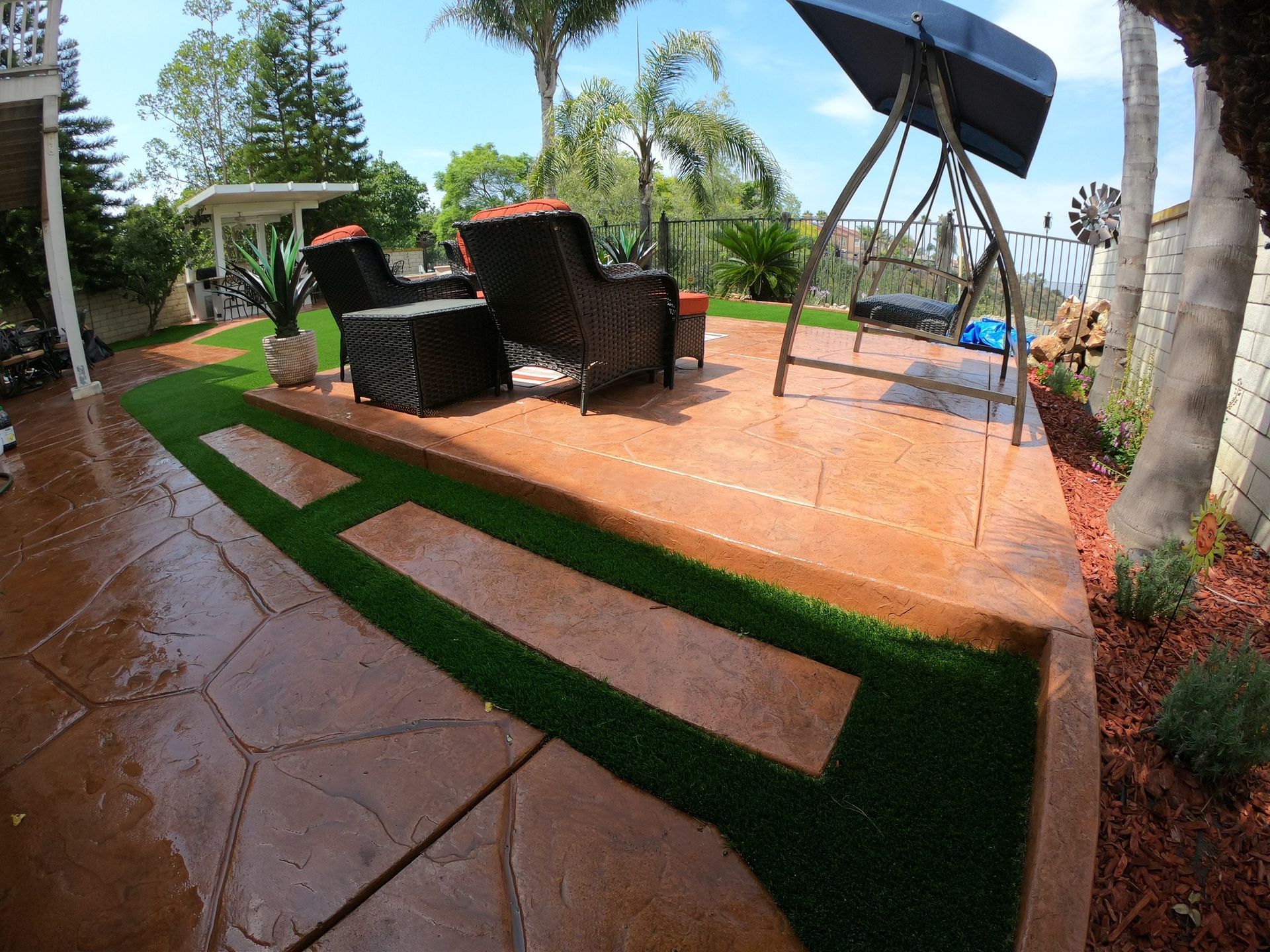 Patio with stamped concrete, artificial turf, and outdoor furniture. Includes a swing and plants.