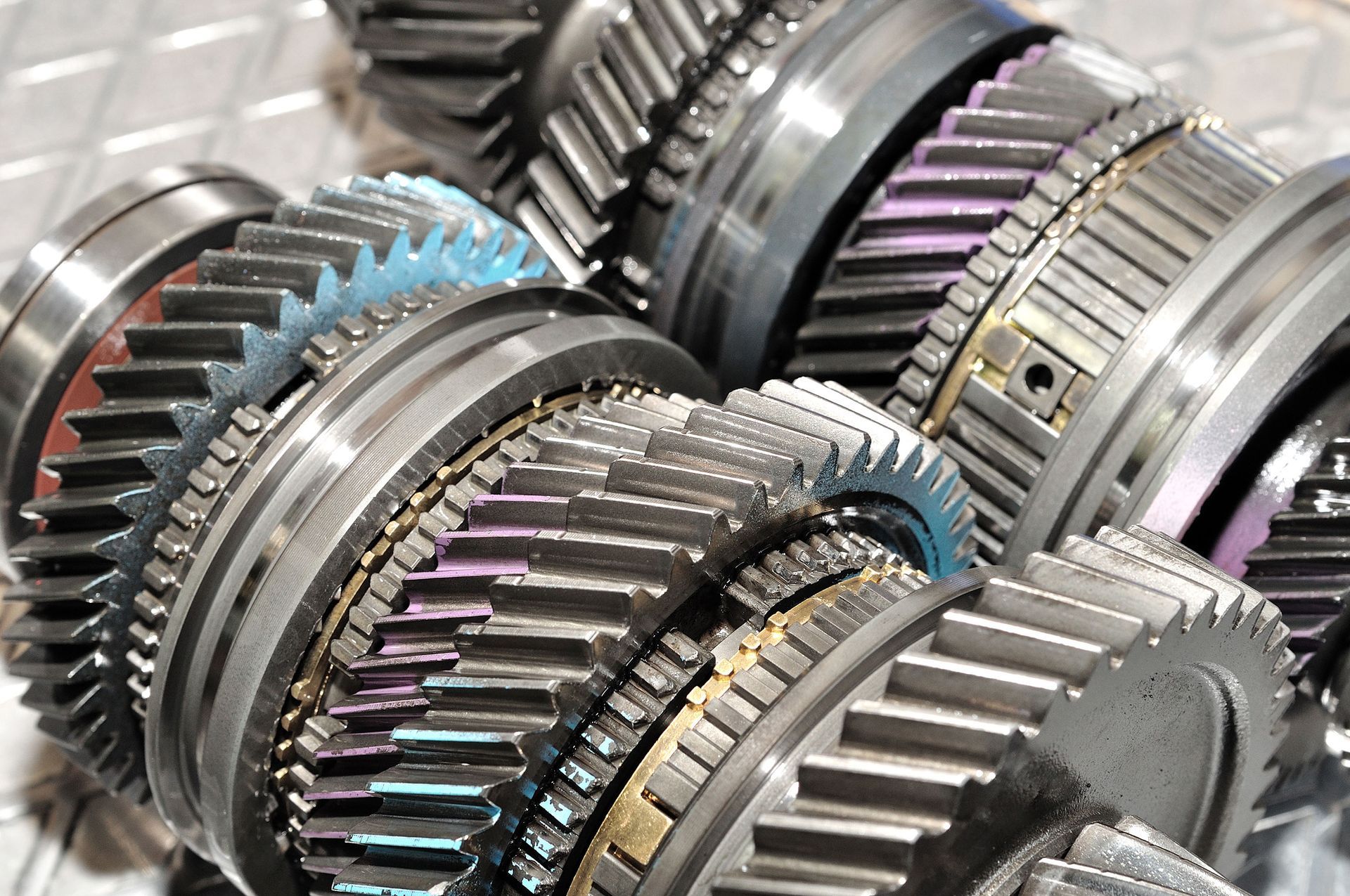 Close-up of several intertwined metal gears, some showing iridescent colors from heat treatment.