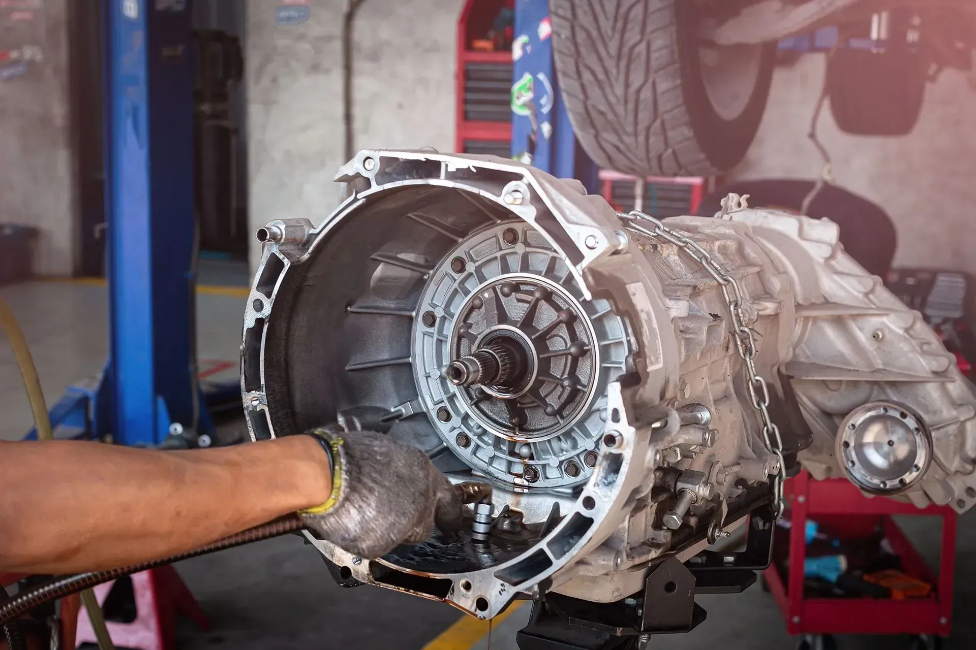 Mechanic's hands working on engine components; gray gears and metal parts visible.