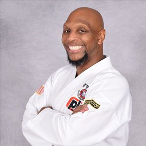 Man in white martial arts uniform, arms crossed, smiling. 