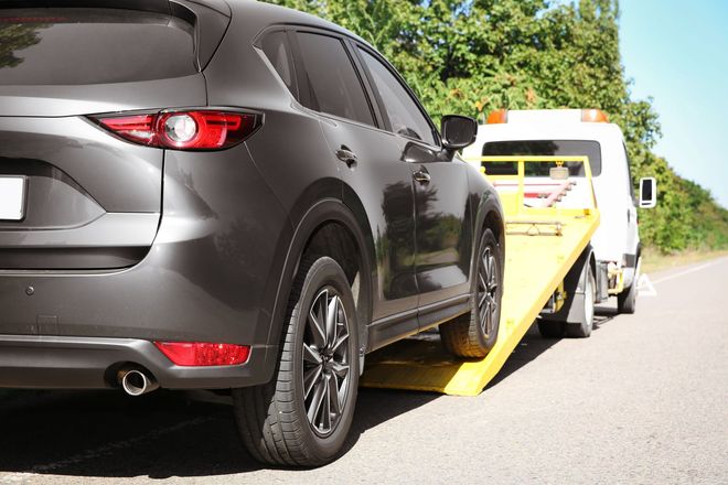 Gray SUV being loaded onto a tow truck on a roadside, with another truck behind it.