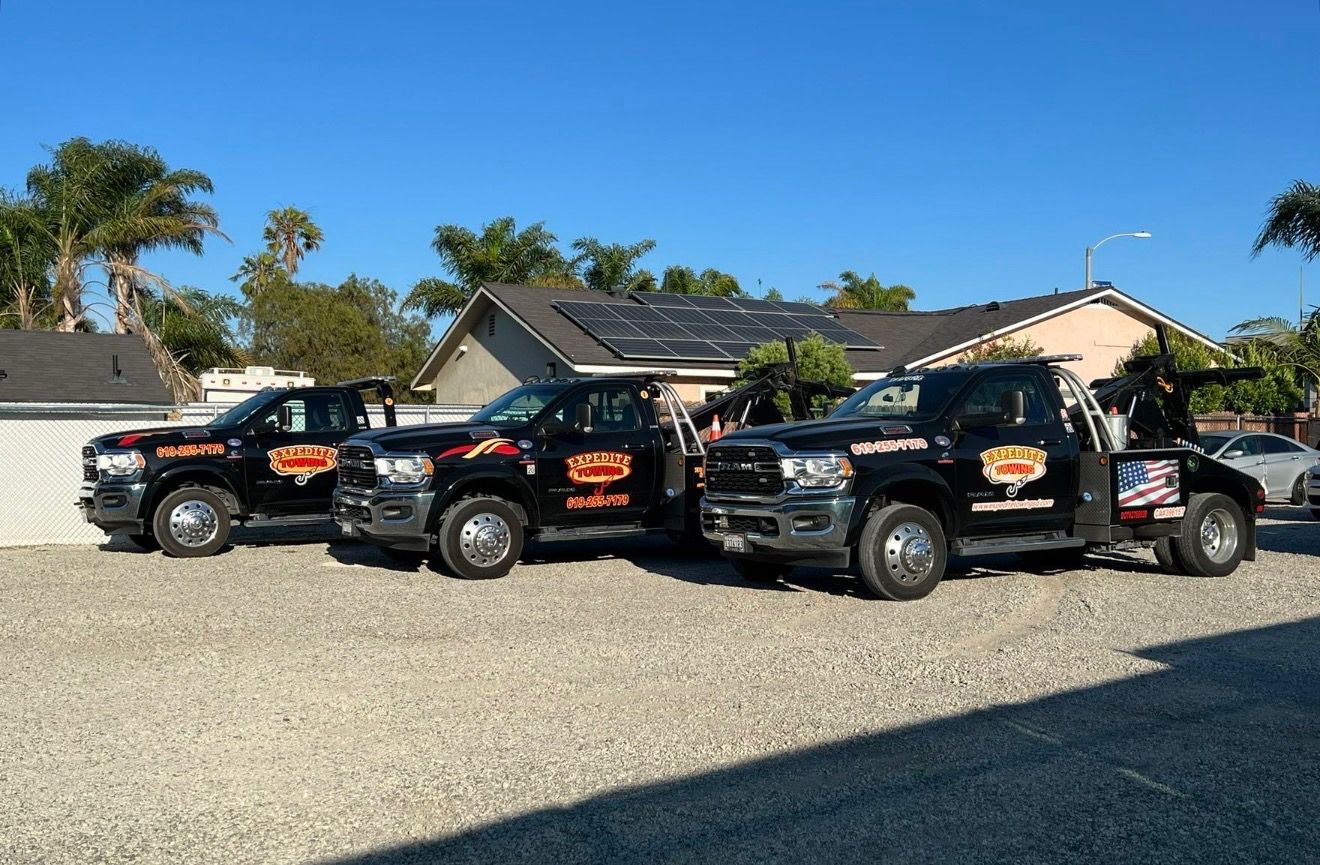 Three black pickup trucks with orange logos parked on gravel in front of houses on a sunny day.