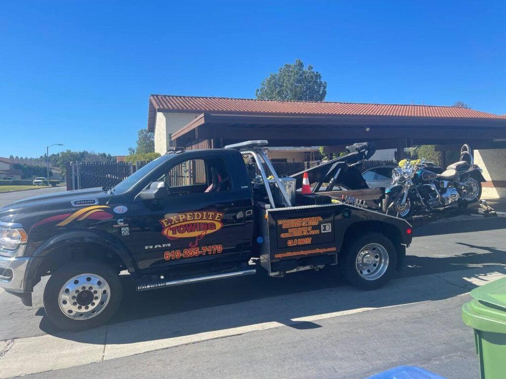 Black tow truck with orange lettering parked under a carport, with a motorcycle in the back.