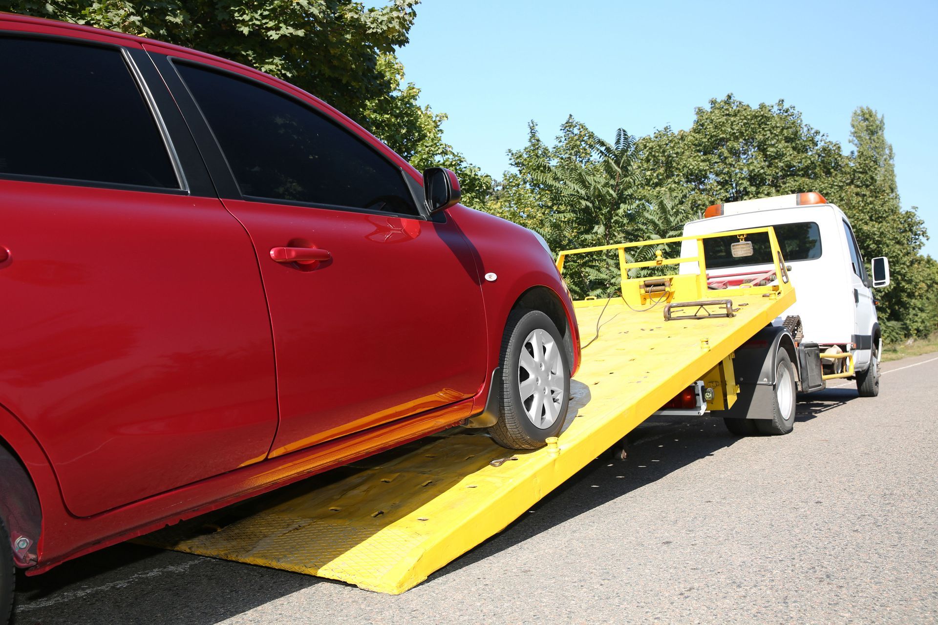 Red car being loaded onto a yellow tow truck on a road, with a white van ahead.