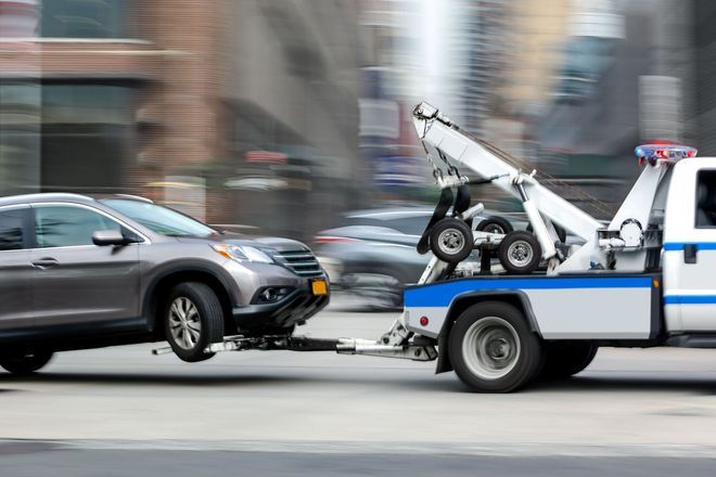 Tow truck towing a gray SUV on a city street, motion-blurred buildings in the background