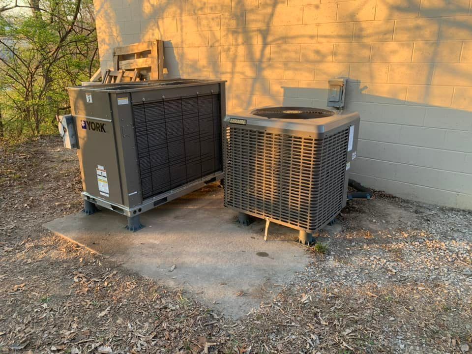 Two air conditioners are sitting next to each other on the side of a building.