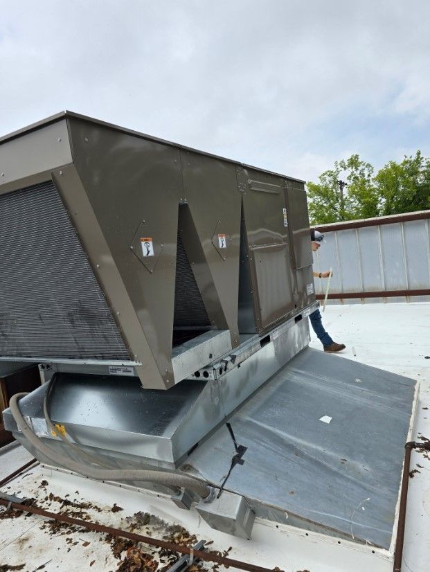A man is standing on a roof next to a large air conditioner.