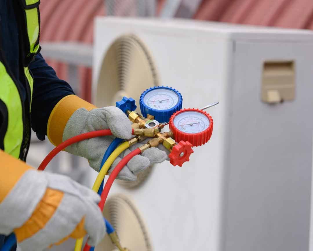A man is holding a couple of gauges in front of an air conditioner.