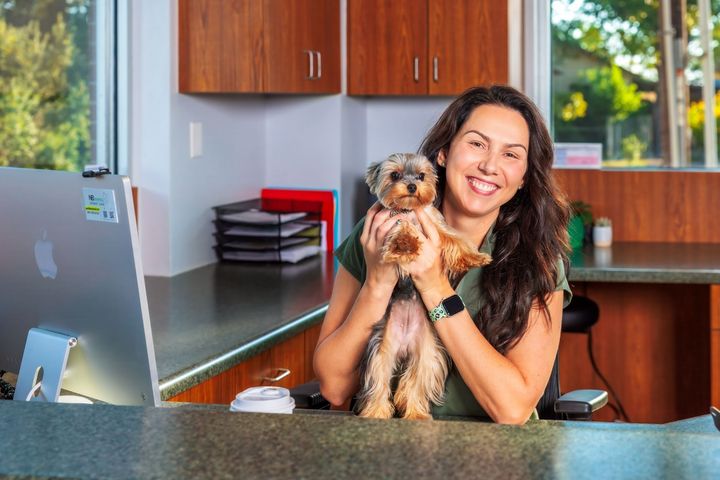 Woman in office holding small dog, smiling.