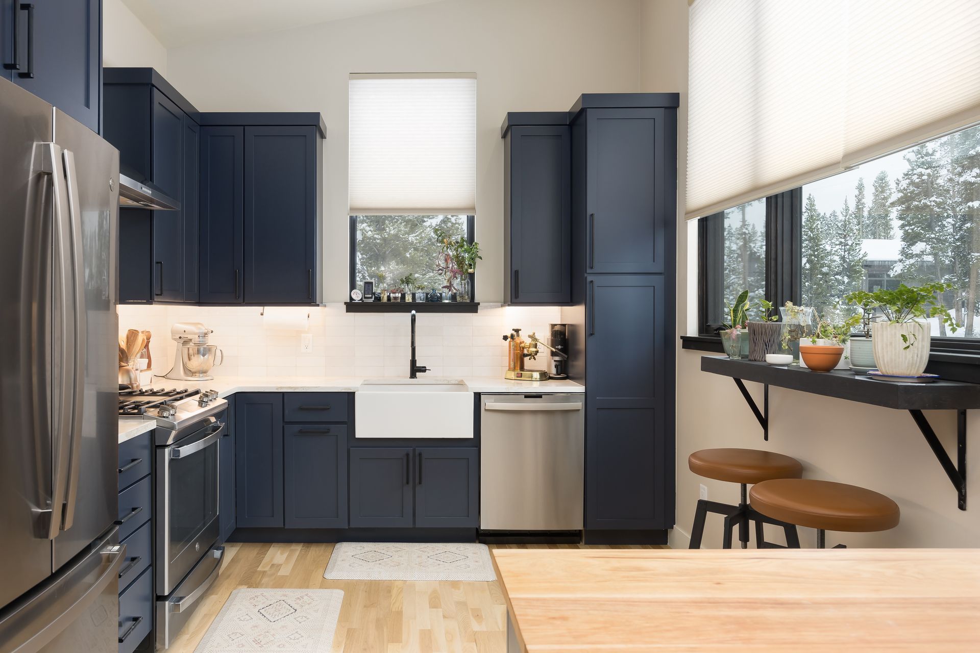 Navy kitchen with stainless steel appliances, white backsplash, and a farmhouse sink.