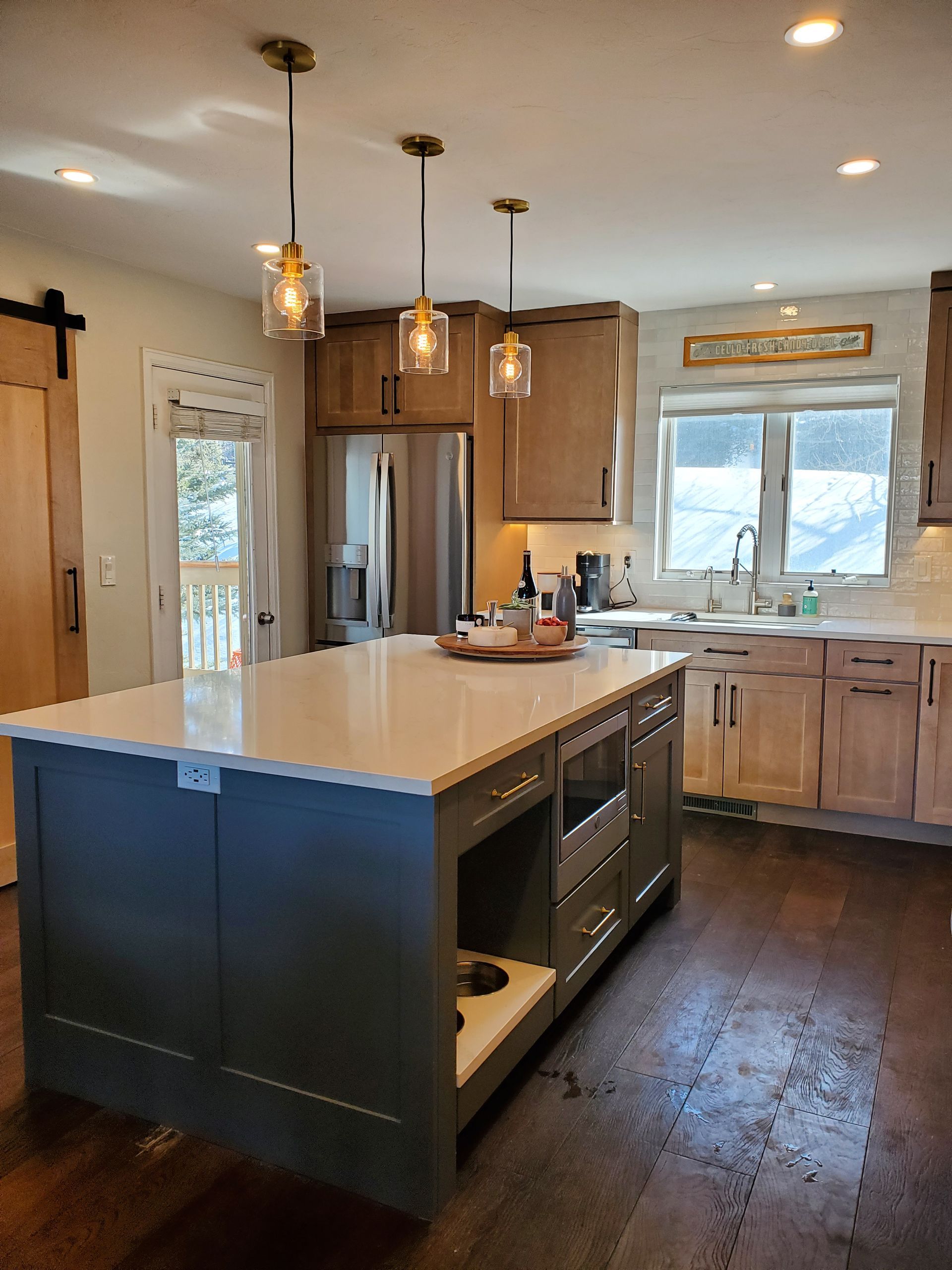 Kitchen with island: grey cabinets, quartz countertop, wooden cabinets, pendant lights, stainless steel appliances.
