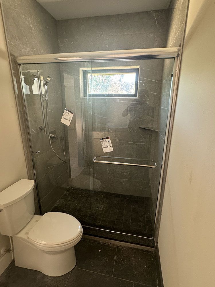 A bathroom with a toilet , shower and sliding glass door.