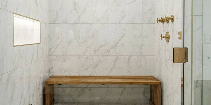 There is a wooden bench in the shower with marble tiles.
