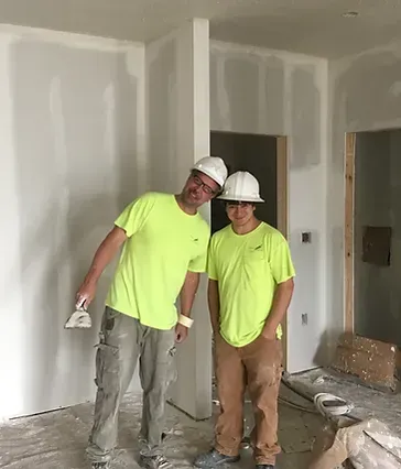 two construction workers are posing for a picture in a room .