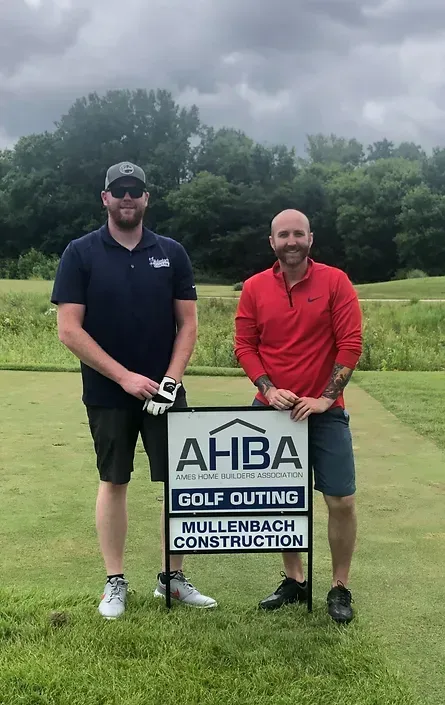 two men are standing next to each other on a golf course holding a sign 