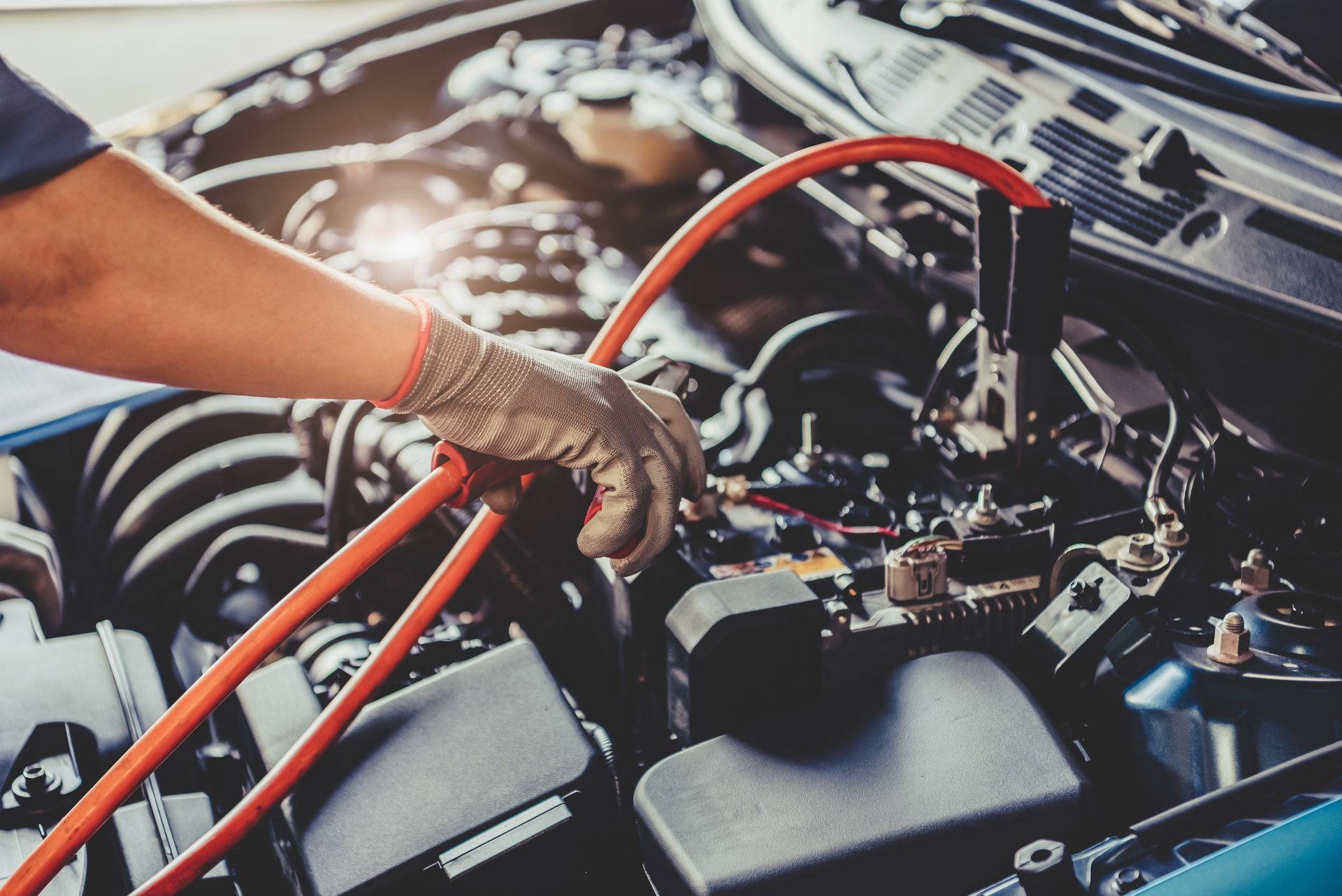 Gloved mechanic inspecting car engine with red jumper cables attached