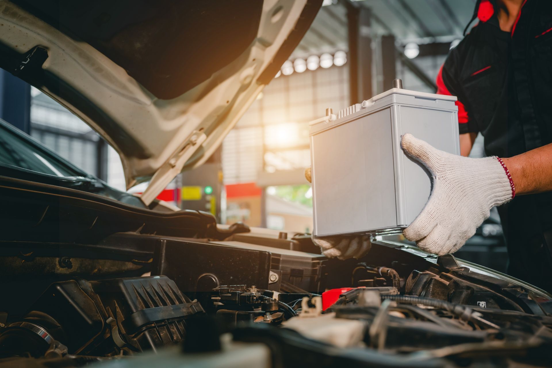 Mechanic inspecting car engine in a garage, holding a white diagnostic box under the hood.