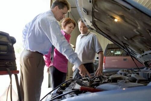 Three people examining a car engine with the hood open in a garage