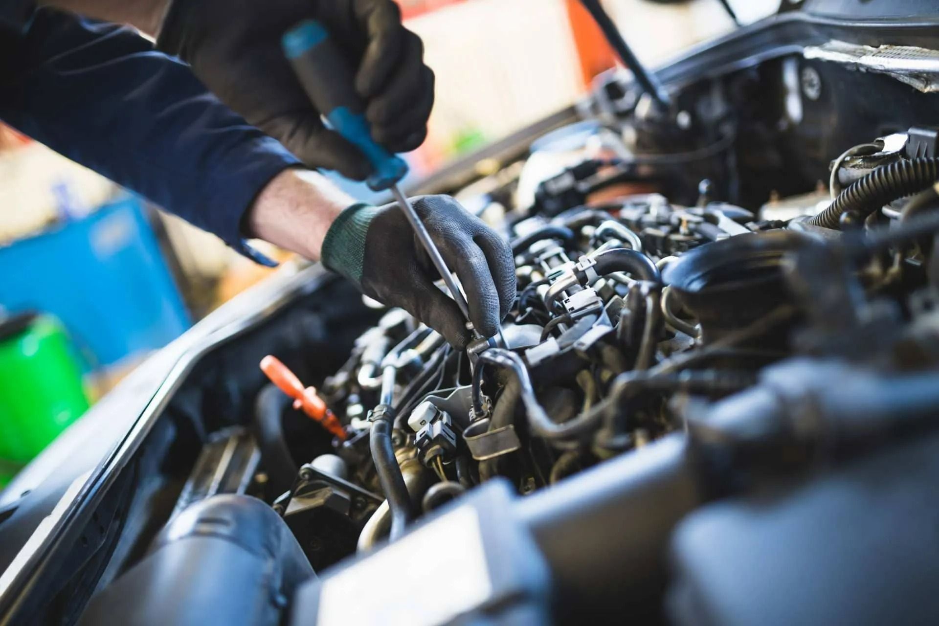 Mechanic working under a car hood with tools in an auto repair shop