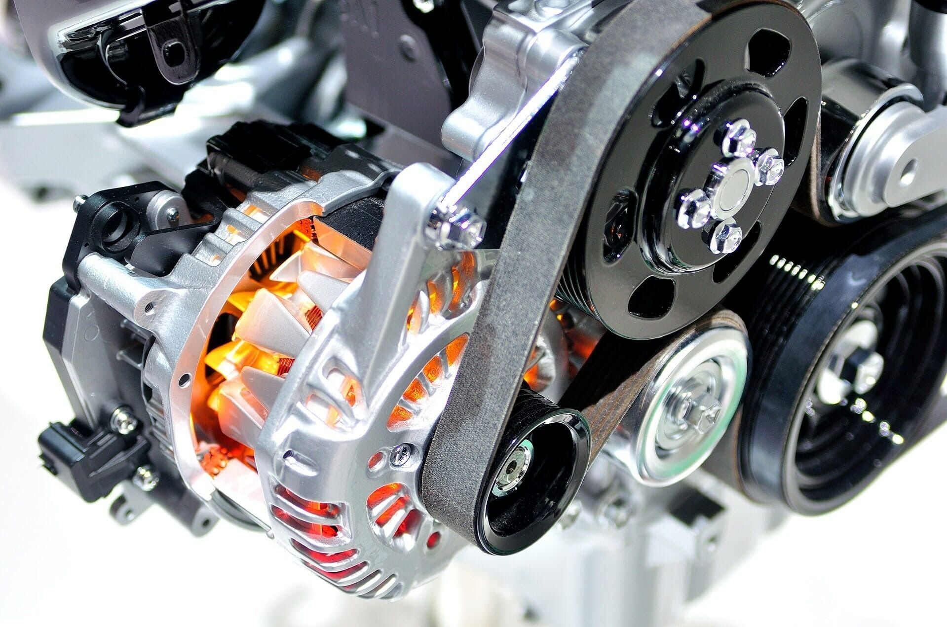 Close-up of a car engine with visible silver pulleys, black belts, and orange-lit components