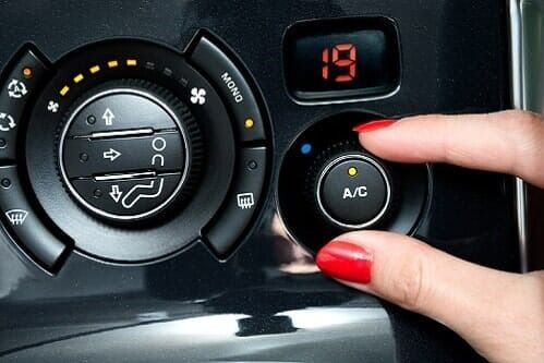 Finger pressing A/C button on a car climate control panel with a red digital display showing 19.