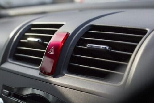 Car dashboard air vents with a red hazard light button in the center