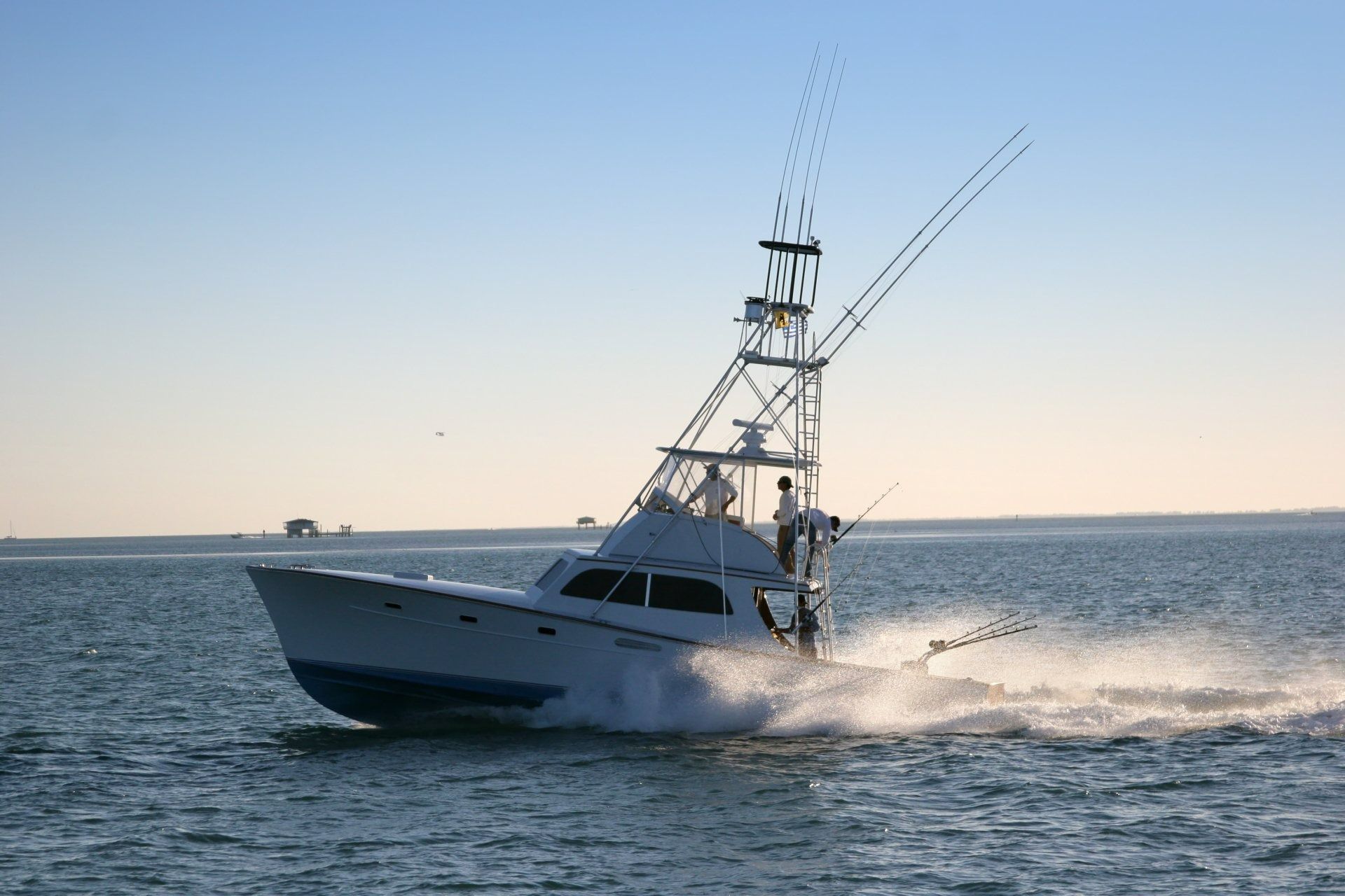 White fishing boat speeding across calm blue water at sunset