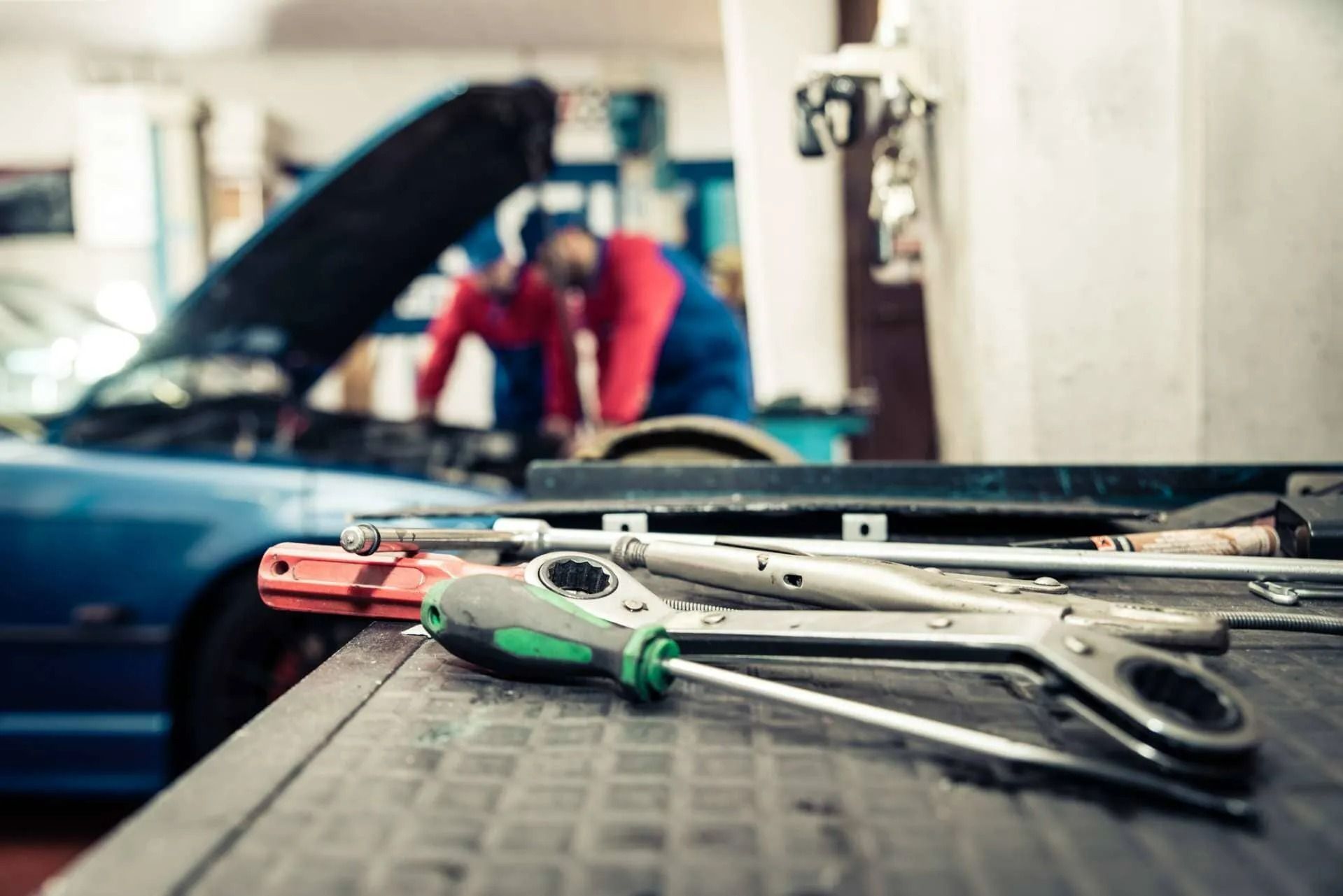Wrenches and screwdrivers on a workbench, with a car and mechanic blurred in the background