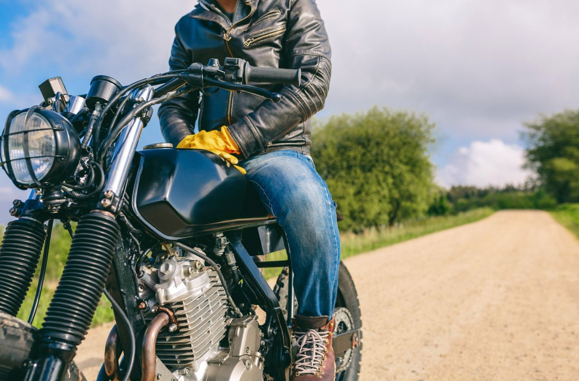 Person on a motorcycle on a rural dirt road with trees and open sky