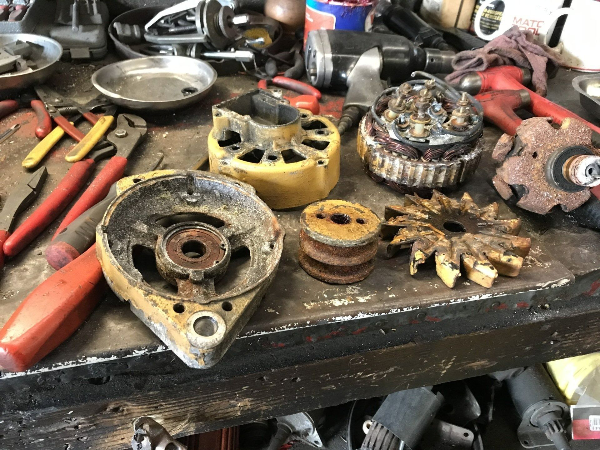 Workbench covered with disassembled rusty metal engine parts and tools in a cluttered repair shop.