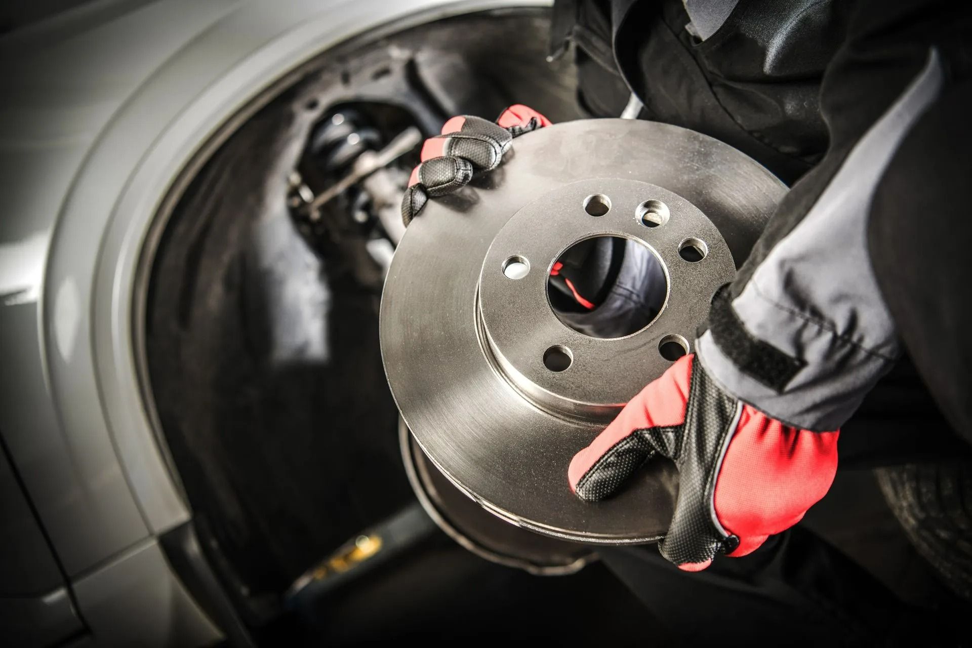 Gloved hands holding a brake rotor beside a car wheel hub in a garage