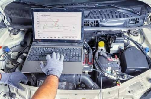 Mechanic using a laptop to diagnose a car engine in an open hood bay