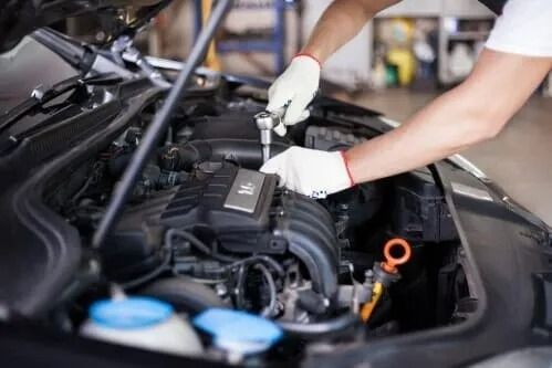 Mechanic wearing gloves working on a car engine in an auto repair shop