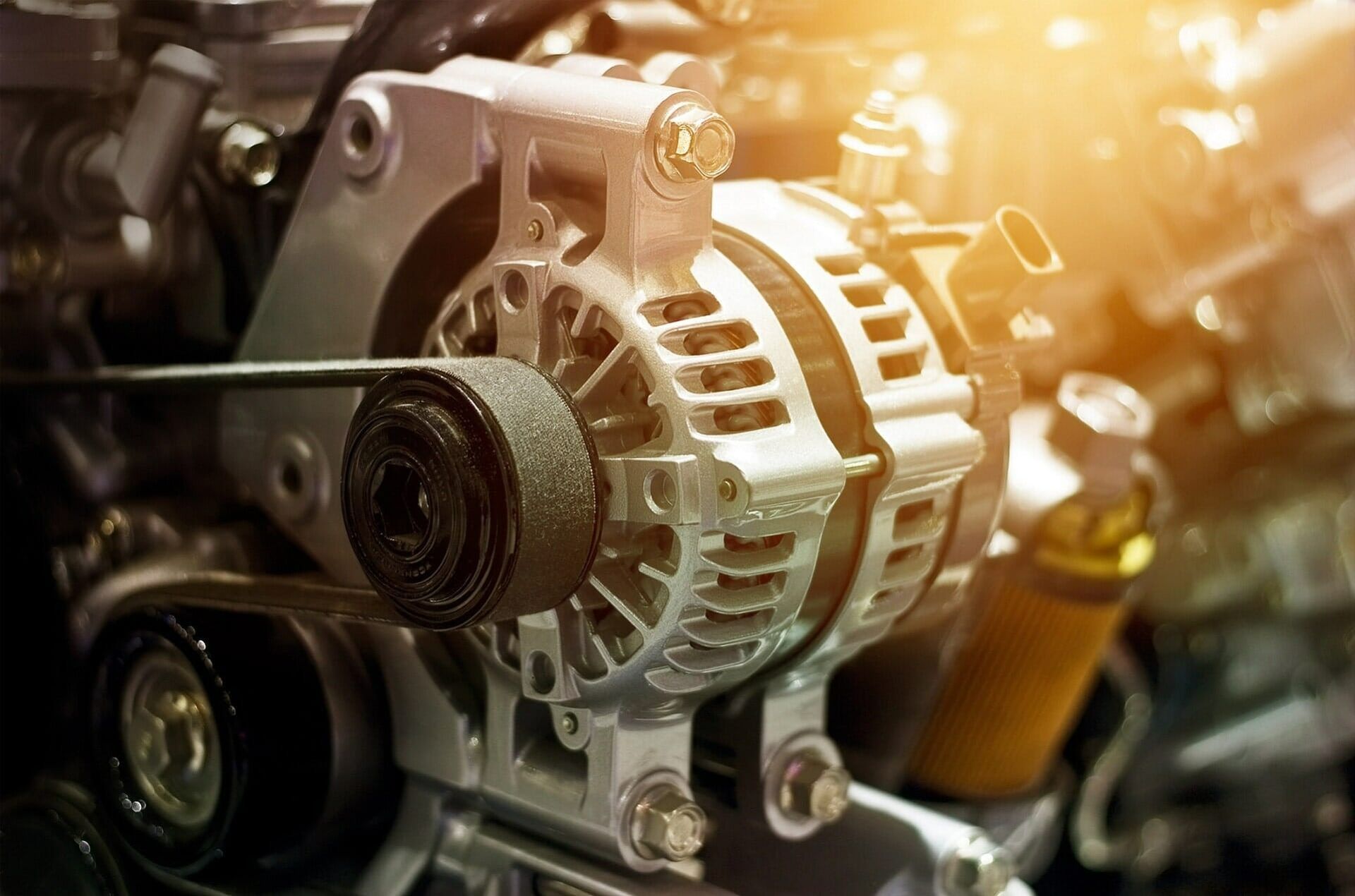 Close-up of a car engine alternator with belt and metal components, lit by warm sunlight
