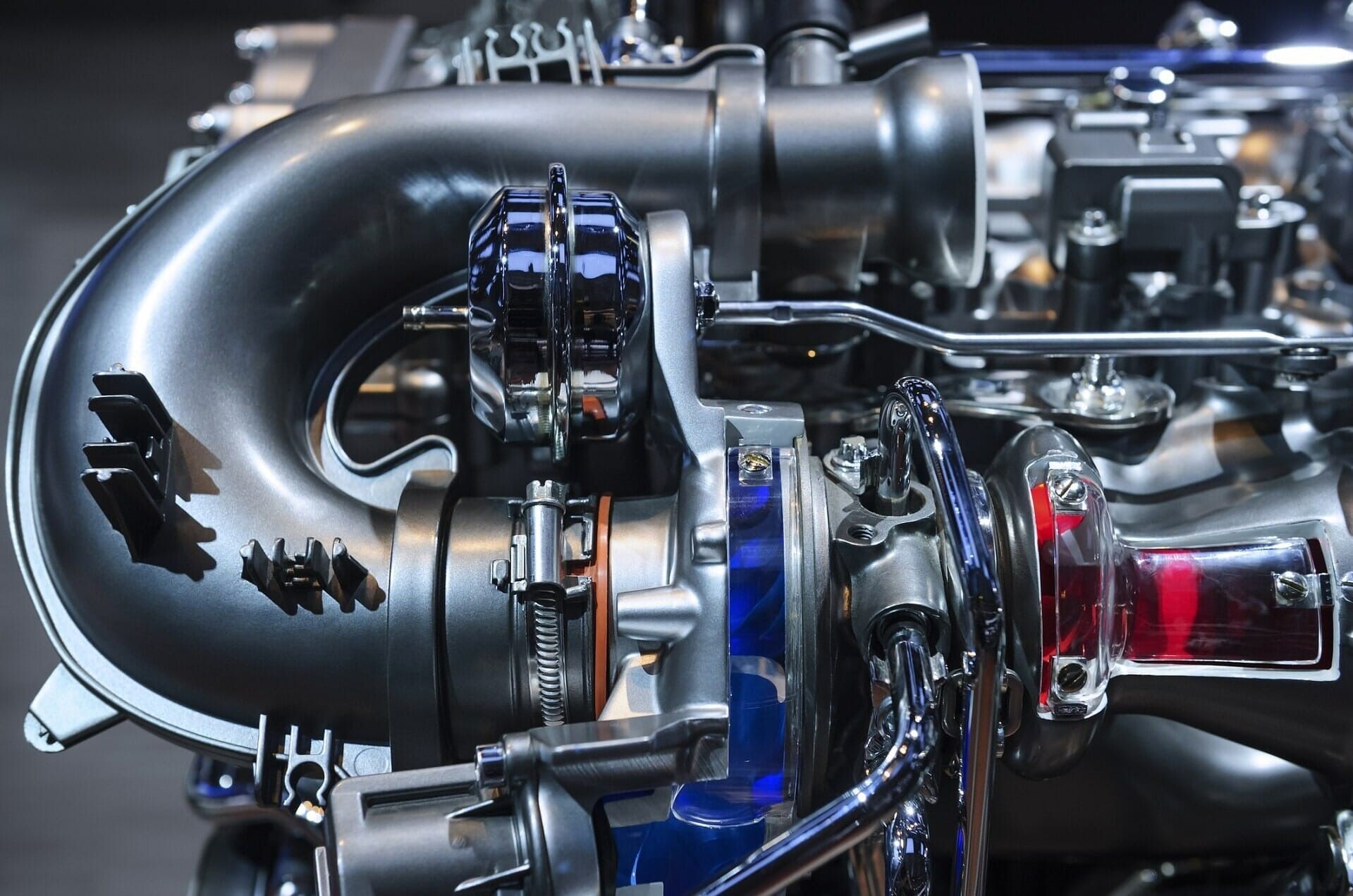 Close-up of a glossy black and blue turbocharger assembly with red intake piping in a car engine bay