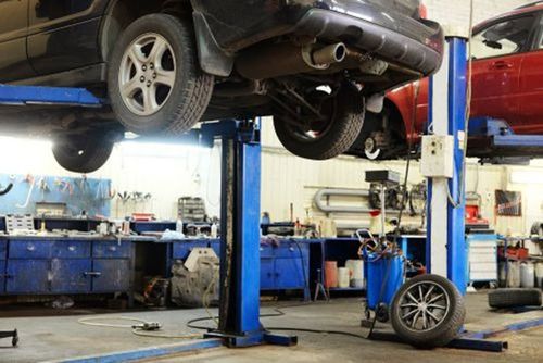 Car elevated on a lift in an auto repair shop, with a mechanic’s tools and a loose wheel nearby