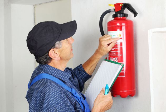 Person inspecting a red fire extinguisher while holding a clipboard
