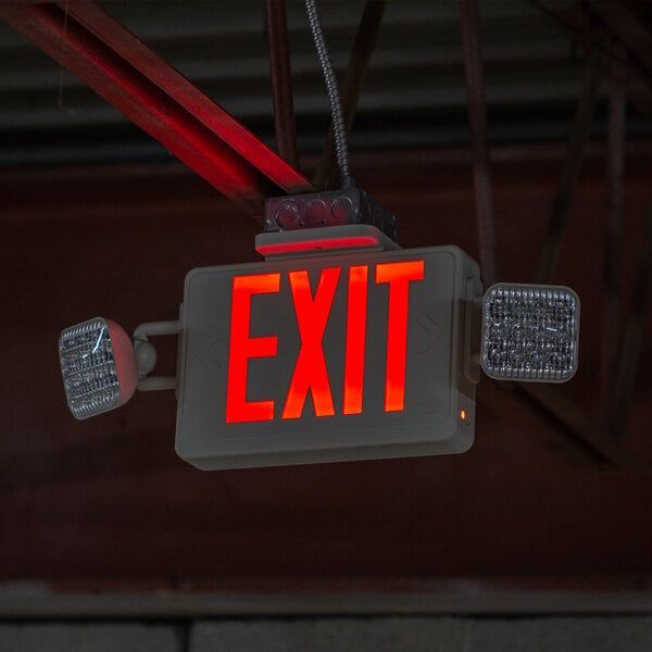 Red illuminated EXIT sign hanging from the ceiling with two side lights in a dark interior.