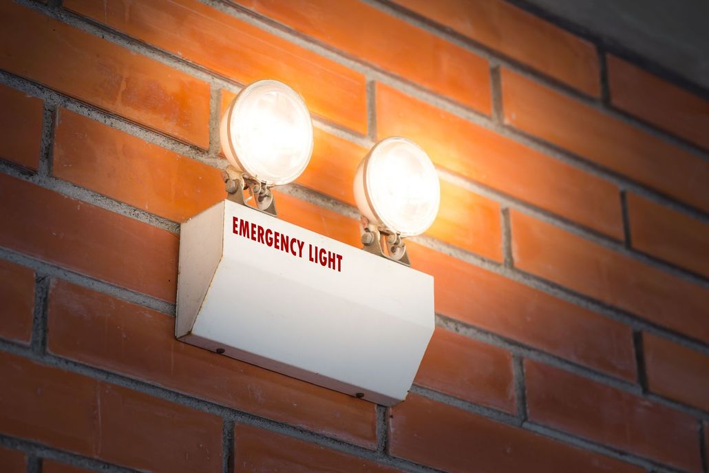 Two lit emergency lights on a white box mounted on a brick wall