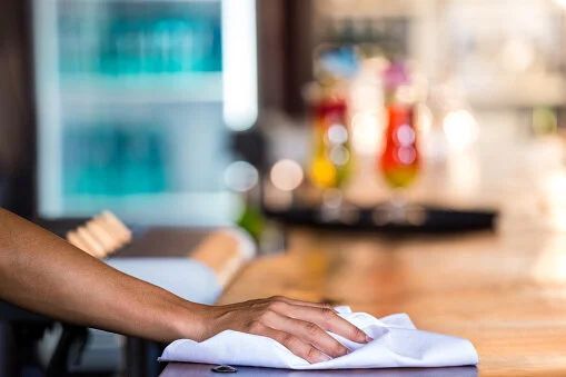 Hand wiping a counter with a white cloth in a blurred kitchen or café setting