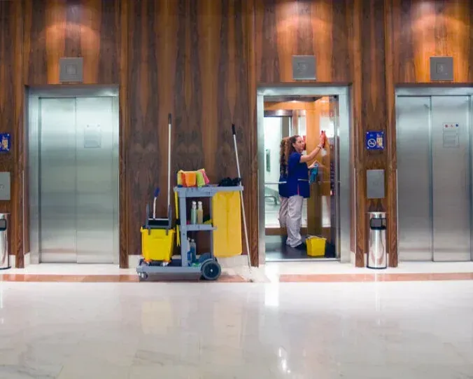 Elevator lobby with two closed elevators and a worker cleaning inside the middle elevator