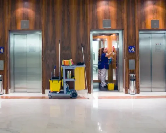Elevator lobby with wood walls, two stainless elevators, and a janitor cleaning the center doorway.