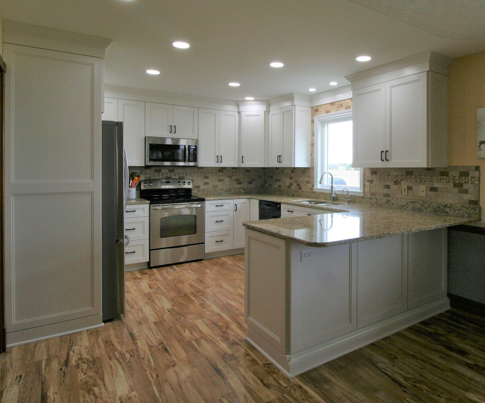 Modern white kitchen with stainless steel appliances, granite countertops, and wood-look flooring.